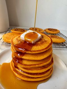 a stack of pancakes covered in syrup on top of a white plate next to a cooling rack