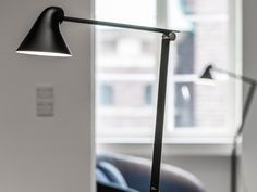 a desk lamp sitting on top of a wooden table next to a chair in front of a window