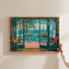 a woman is holding up a painting on the wall with an open window and palm trees