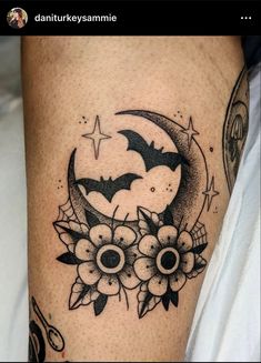 a black and white tattoo on the leg of a woman's legs with flowers and bats