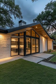 a modern house with glass doors and windows on the front lawn at night, surrounded by trees