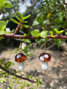 two small red and white earrings hanging from a tree branch in the woods with green leaves