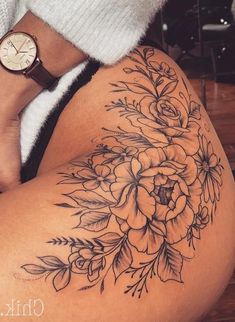 a woman's thigh with flowers on it and a watch in her hand behind her