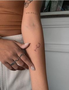 a woman's arm with a wine glass tattoo on her left arm and the word balance written in cursive writing