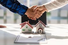 two people shaking hands over small houses on top of a table in front of a laptop