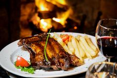 a white plate topped with meat and french fries next to a glass of red wine