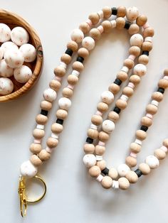 a wooden bead necklace next to a bowl of white and black beads on a table