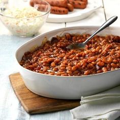 a large white bowl filled with baked beans and hot dog buns in the background