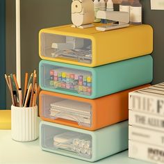 a stack of four plastic containers sitting on top of a desk next to books and pencils