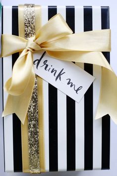 a black and white striped present box with a gold ribbon that says drink me on it