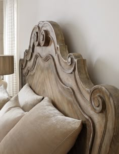 a large wooden headboard sitting on top of a bed next to a lamp and window