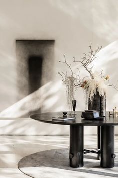 a table with vases and flowers on it in front of a white wall,