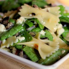 spinach pasta salad with black olives and feta cheese in a white bowl