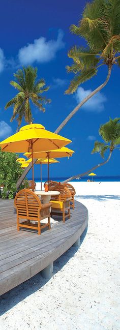 an umbrella and chairs on a wooden deck at the beach with palm trees in the background