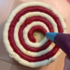 someone is making a pastry with red and white icing in the shape of a spiral