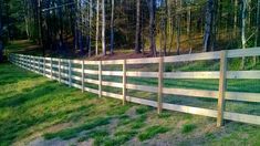 a wood and wire fence in the middle of a grassy area with trees behind it