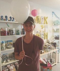 a young man holding two white balloons in his hand and standing next to a book shelf