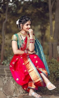 a woman sitting on top of a stone wall wearing a red and blue dress with gold accents