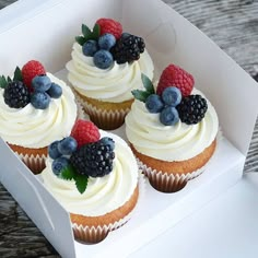 cupcakes with white frosting and fresh berries on top are in a box