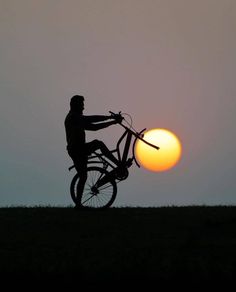 a person riding a bike with the sun setting in the back ground behind them on a hill