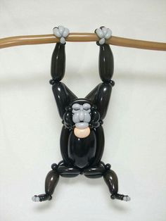 a black monkey figurine hanging upside down on a wooden bar with two hands