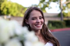 a beautiful young woman standing next to a bouquet of white flowers smiling at the camera