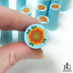 a hand holding a small blue button with a sunflower on it and six smaller ones in the background