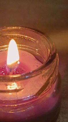 a lit candle sitting in a glass jar on a counter top with water droplets around it