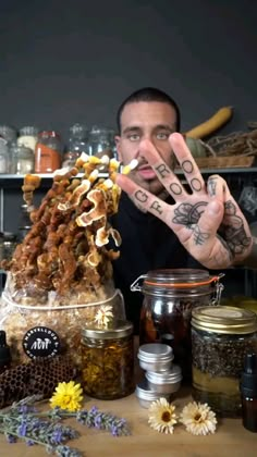 a man with his hands in the air while surrounded by various jars and flowers, including honey