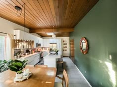 a kitchen with green walls and wood ceilinging next to a wooden dining room table