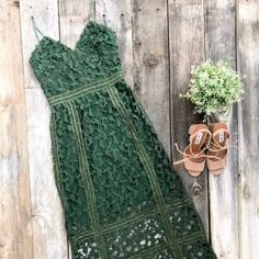 a green crochet dress next to a pair of sandals and a potted plant