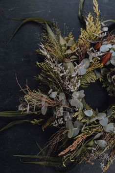 a wreath made out of dried flowers and greenery on a black surface with leaves