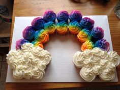 cupcakes with white frosting and rainbow swirls on a cutting board in front of a wooden table