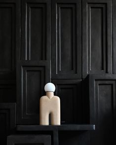 a wooden mannequin sitting on top of a black table in front of wood paneled walls