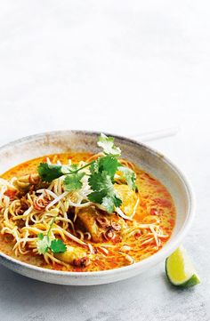 a white bowl filled with soup and garnished with cilantro, parsley and lime