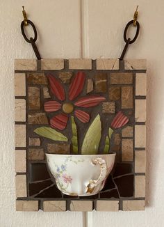 a vase with flowers in it is hanging on a brick wall and has two hooks