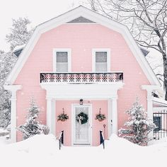 a pink house covered in snow with wreaths on the front door