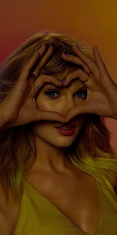 a woman with her hands on her face making a heart shape in front of her eyes