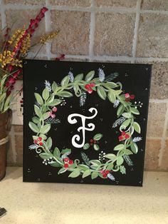 a painted monogram on a black canvas with red berries and green leaves around it