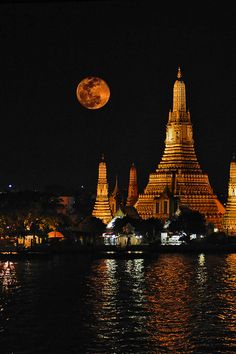 the full moon shines brightly in front of an ornate building on the water's edge