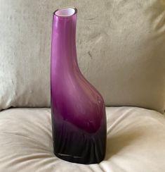 a purple glass vase sitting on top of a white couch next to a pillow and pillows