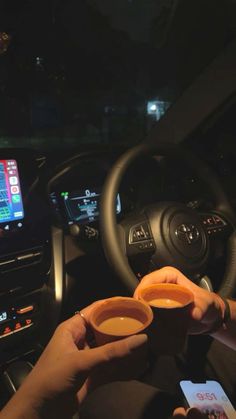 two people holding cups in their hands while driving