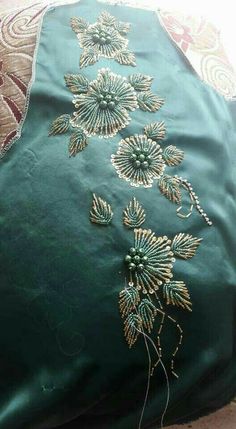 a green pillow with gold embroidered flowers on the front and back, sitting on top of a rug