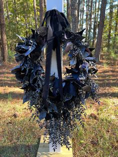 a wreath made out of black leaves in the grass with trees in the back ground