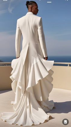 a man in a white suit standing on top of a roof next to the ocean