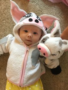 a baby is wearing a pig costume and holding a stuffed animal in her arms while standing on the floor