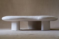 a white bench sitting on top of a floor next to a beige wall with no one around it