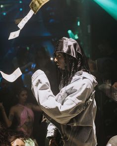 a man with dreadlocks standing in front of a crowd and throwing papers into the air