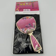 a pink and gold mirror with flowers on it in a plastic packaging bag next to a white background