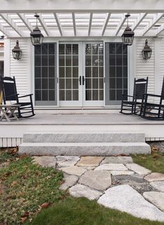 a porch with rocking chairs on it next to a door and steps leading up to the front door